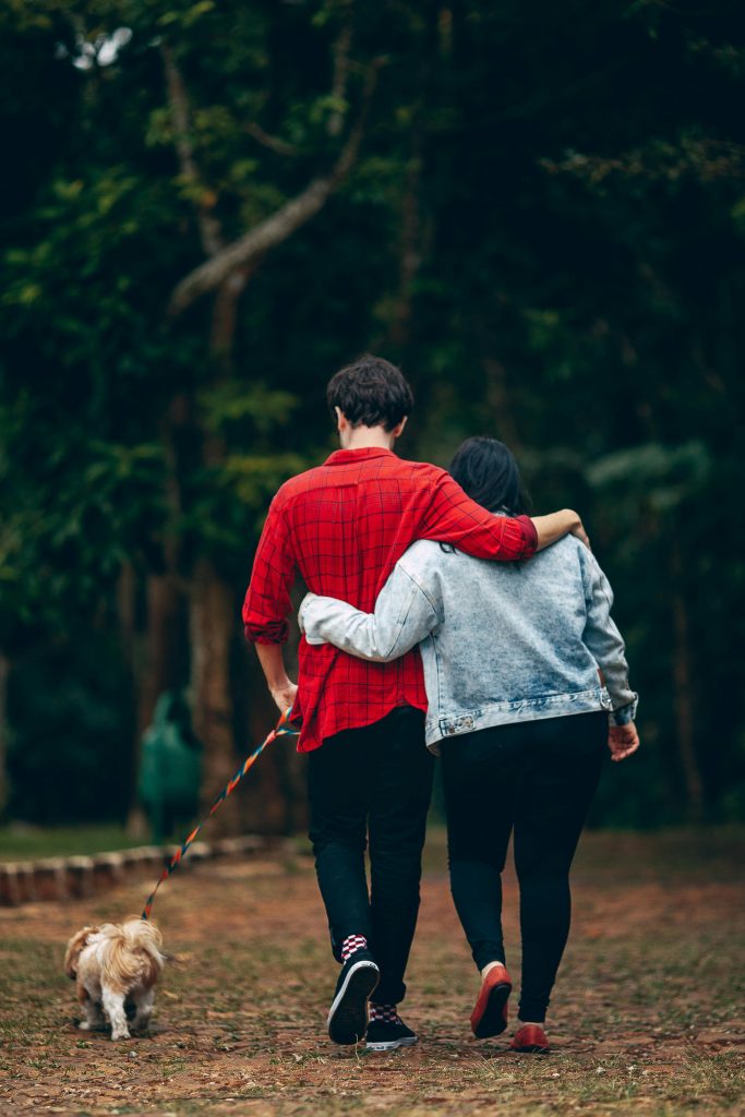 Couple walking with a Shih Tzu in a lush park, embracing affectionately.