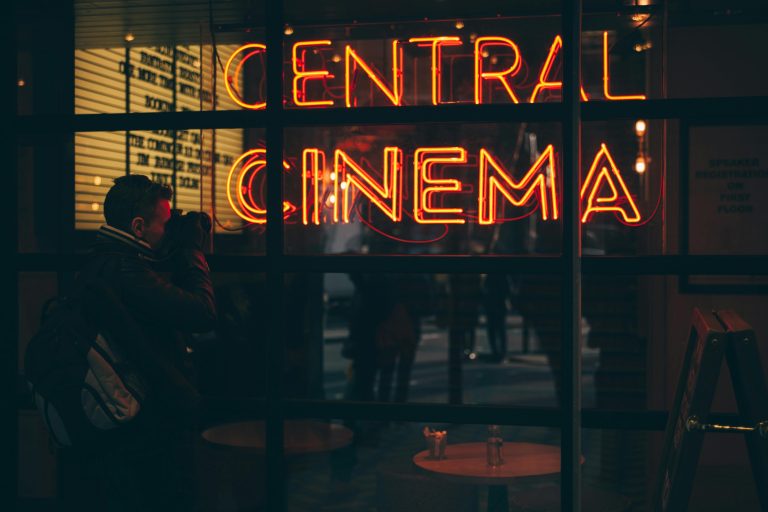 A photographer captures the vibrant neon glow of a cinema sign during the evening.